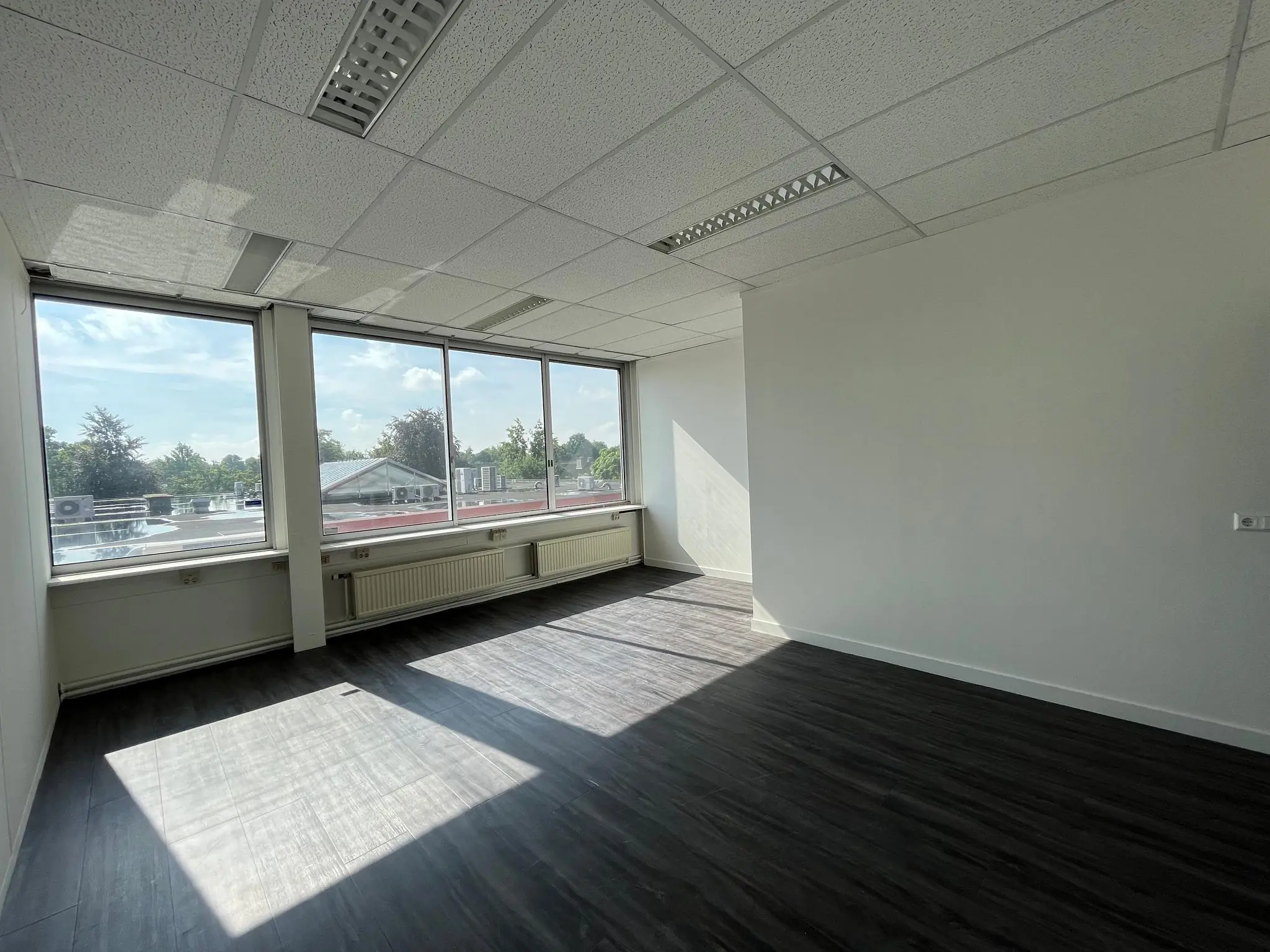 Licht kantoorruimte met donkere vloer en grote ramen aan de Jan van Eycklaan.